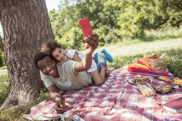 Hombre de piel oscura haciendo selfie con su hija pequeña en el parque - Foto, Imagen