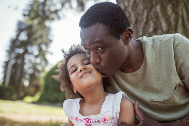Dark-skinned man kissing his little kid and feeling happy - 写真・画像