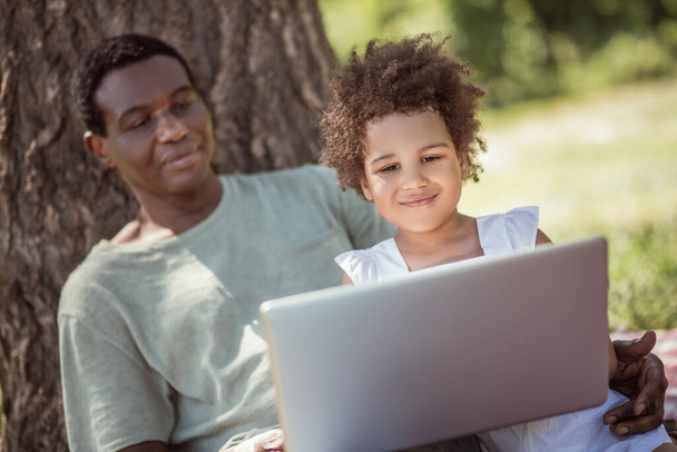 Curly-haired little girl and her dad watching something on laptop - Foto, Bild
