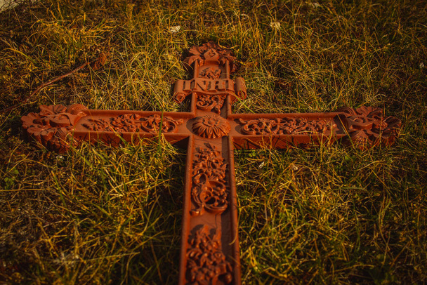 Crucifijo de metal olvidado y caído sin Jesús, renovado en color marrón pero luego olvidado, acostado en la hierba. Concepto de religión olvidada o rituales. - Foto, imagen
