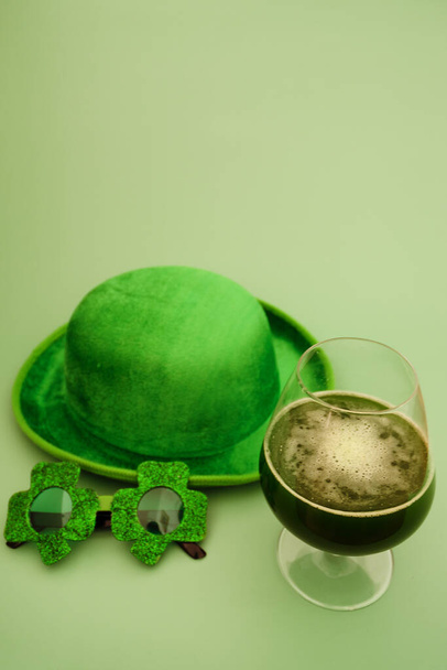 Feliz concepto del Día de San Patricio. Un vaso de cerveza verde. Gafas de fiesta y sombrero en fondo verde. Tarjeta de felicitación. Copiar espacio. Vista superior.  - Foto, Imagen