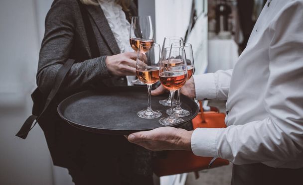 Persone che prendono bicchieri di vino rosato da un vassoio tenuto da un cameriere professionista o catering. Ristorazione con vino su un evento aziendale all'interno. - Foto, immagini