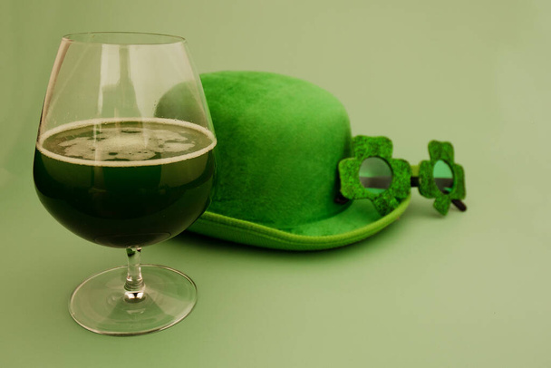 Happy St Patrick's Day concept. Glass of green beer. Party glasses and hat in green background. Greeting card. Copy space. Top view.  - Photo, image