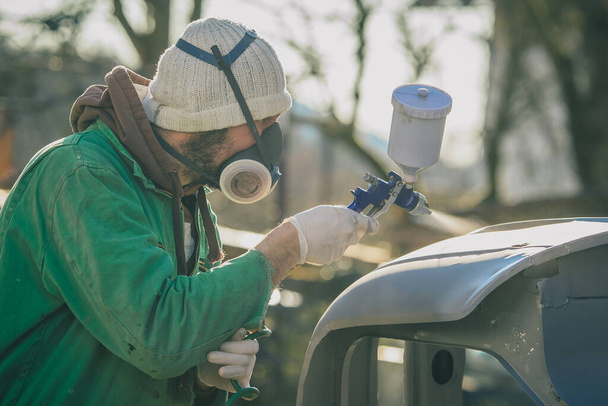 Egy férfi autóipari légfúvó pisztollyal bevetés közben egy veterán autó felújításakor. Az első alapréteg festék alkalmazása csupasz fémre. - Fotó, kép