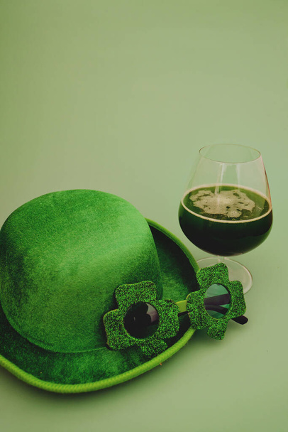 Boldog Szent Patrik-napot! Egy pohár zöld sört. Parti szemüveg és kalap zöld háttérben. Üdvözlőlap. Másold a helyet. Felülnézet.  - Fotó, kép