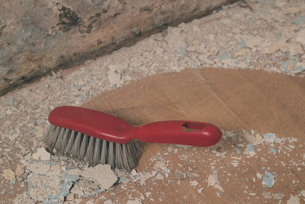 Red plastic broom sweeping away debris fallen from an old wet mossy wall down onto laminate floor. Visible clean path behind. - Photo, Image