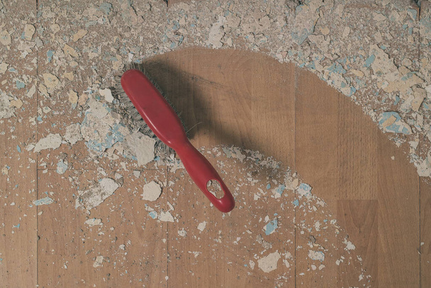 Vassoura de plástico vermelho varrendo detritos caídos de uma antiga parede molhada musgosa para baixo no chão laminado. Caminho limpo visível atrás. - Foto, Imagem