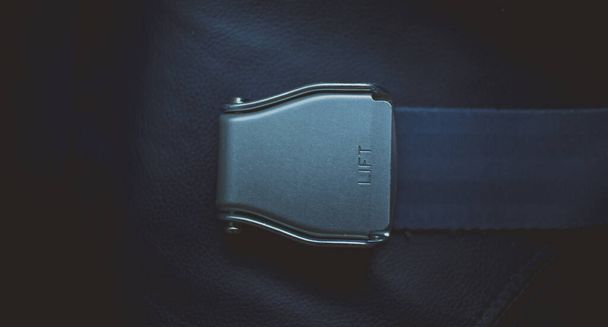 Aeroplane seatbelt buckle in low key dark moody photo. Artistic or different photo of a seatbelt buckle sitting on a chair made of leather. - Photo, Image