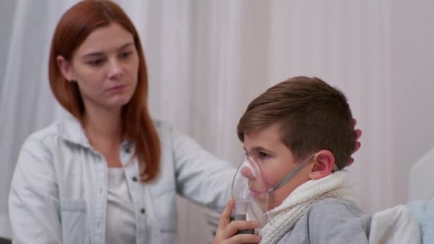 μητέρα ανησυχεί για την υγεία του αρσενικού παιδιού της με συμπτώματα πνευμονίας και βοηθά το γιο της εισπνευστήρα στο σπίτι στο κρεβάτι - Πλάνα, βίντεο