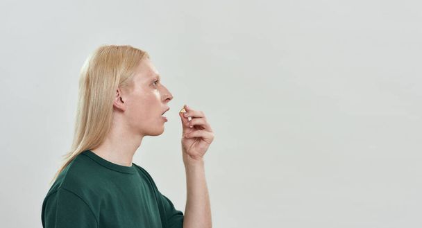 Young caucasian boy swallowing pill on light background - Фото, изображение