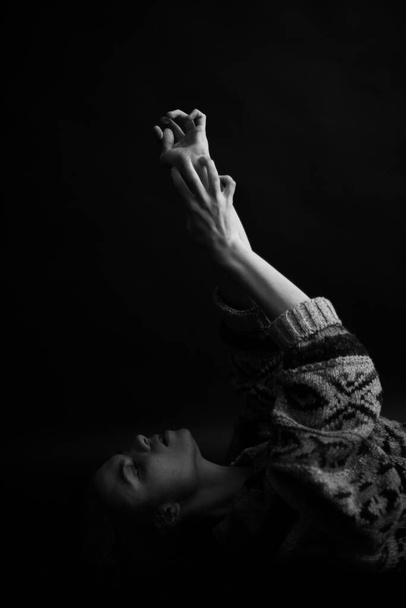 brunette girl with voluminous sweater moves freely and dances, art portrait of a dancer on a black background - Fotó, kép