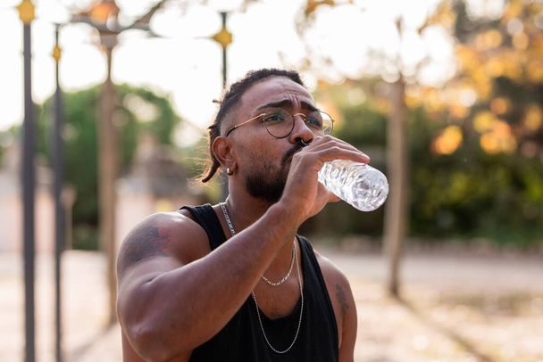 Afrikkalainen amerikkalainen urheilija poika tatuointi juo vettä pullosta puistossa. - Valokuva, kuva
