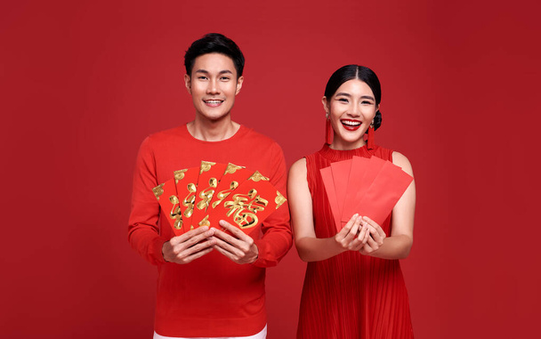Happy asian couple in red casual attire with holding angpao or red packet monetary gift of congratulation greeting happy new year 2021 on bright red background. text means great luck.  - Photo, Image