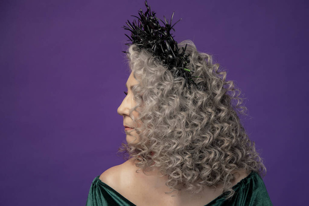 Portrait studio d'une femme âgée de 60 à 65 ans dans une belle robe avec une couronne sur la tête sur un fond coloré. Concept : pensionnés élégants d'apparence modèle, vie active. - Photo, image
