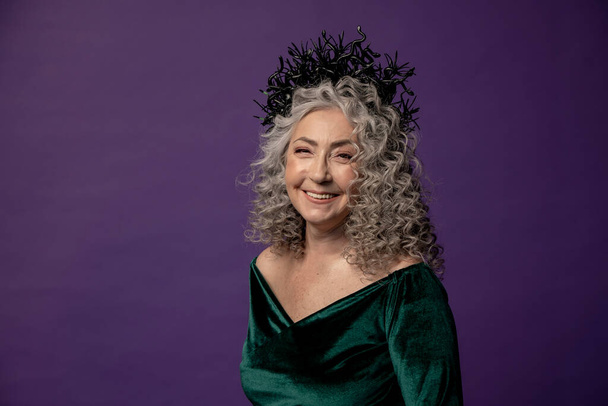 Studio portrait of an elderly woman 60-65 years old in a beautiful dress with a crown on her head on a colored background. Concept: stylish pensioners of model appearance, active life. - Photo, Image