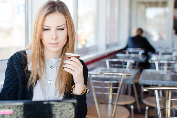 Femme mignonne assise dans un café à boire du café et de travailler sur un ordinateur portable
 - Photo, image