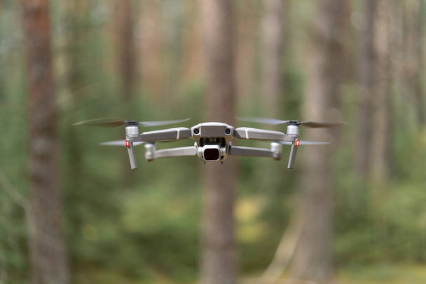 飛行中に地面の上にNDフィルターホバーを備えたカメラ付きのドローン用クワッドコプター。森の中の無人航空機。畑の浅い深さ、背景のぼやけている. - 写真・画像