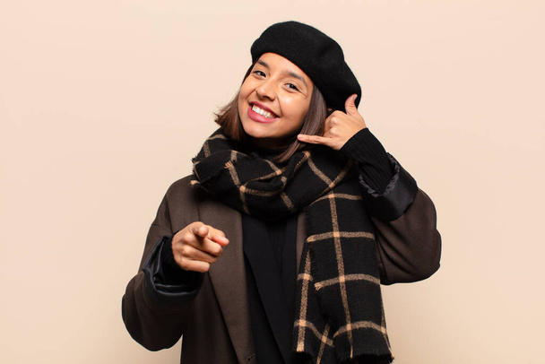 hispanic woman smiling cheerfully and pointing to camera while making a call you later gesture, talking on phone - Foto, immagini