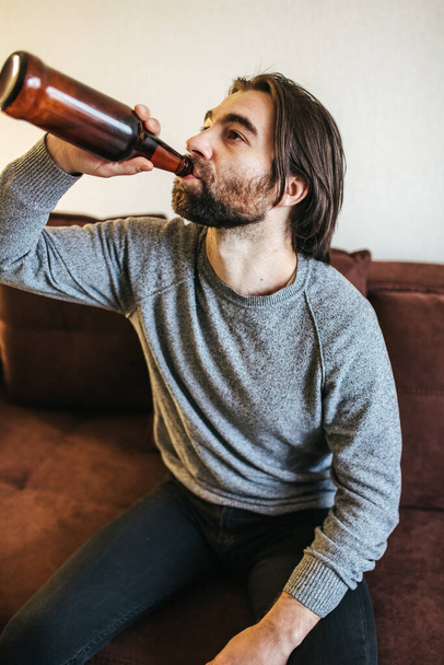 Alcohol addiction at young age. Caucasian male cannot stop drinking alcohol, drunken lonely male drinks from bottle. Loneliness, depression and alcoholism during Christmas and New Year holidays - Fotoğraf, Görsel