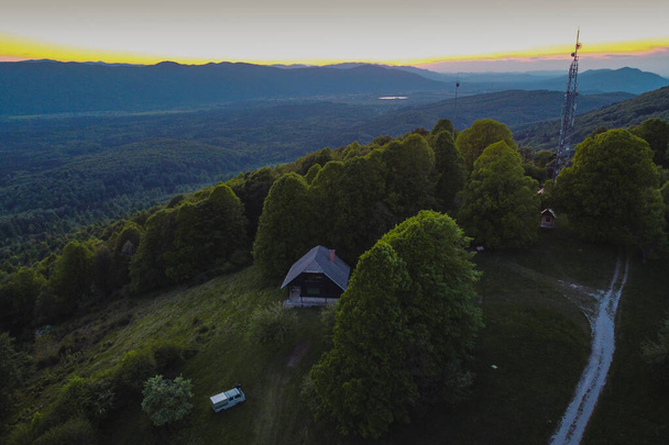 日没または夕方の間にスロベニアのコチェフスコ地方のバンで野生のキャンプ。山の小屋とアンテナが見えるコチェフェ周辺の丘の美しいパノラマ. - 写真・画像