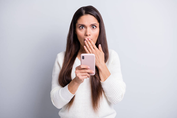 Φωτογραφία του ώριμου σοκαρισμένος έκπληκτος όμορφη γυναίκα κάλυψη στόμα κρατήσει smartphone απομονωμένο σε γκρι φόντο χρώμα - Φωτογραφία, εικόνα