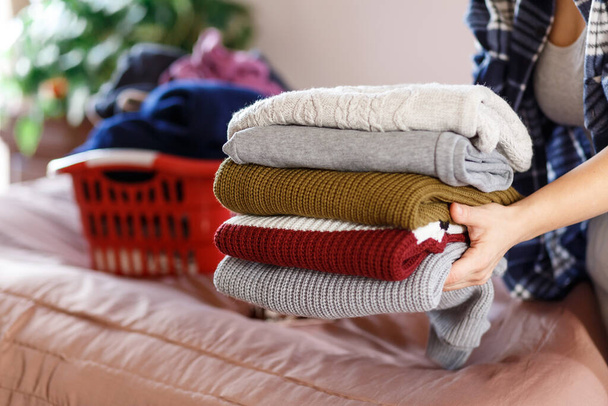 Mujer manos doblando la ropa, suéteres acogedores de punto en un dormitorio, recoger después de lavandería.concepto de ama de llaves - Foto, imagen