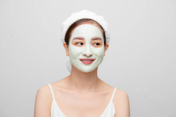 Odosobnione ujęcie ładnej kobiety nosi maskę na twarz dla odświeżenia skóry ręcznikiem na białym tle. - Zdjęcie, obraz