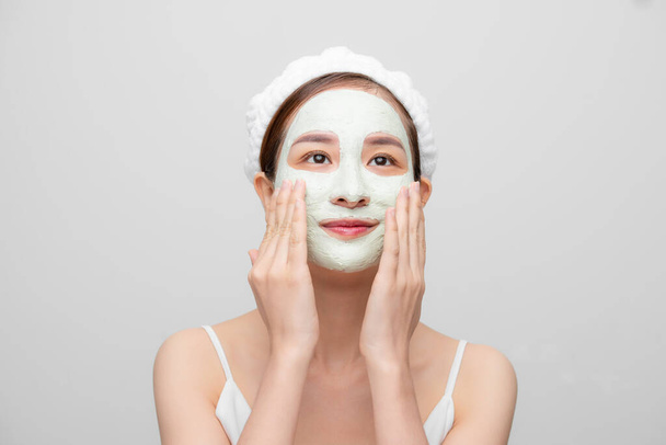 Spa teen Asian girl applying facial clay mask. Beauty treatments. Over white background. - Foto, afbeelding