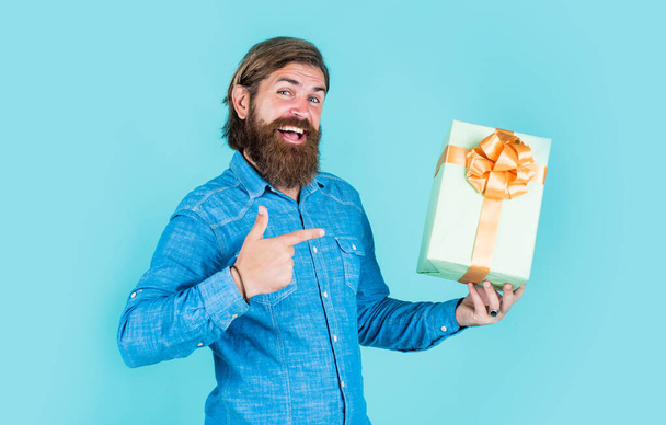 successful shopaholic in shirt. bearded man ready for holiday. sale and discount. mature hipster with beard pointing finger on present box. brutal caucasian hipster with gift. male go shopping - Foto, afbeelding