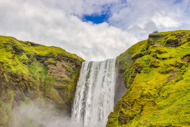 A closeup shot of a waterfall in the greener in Iceland under a cloudy sky - Foto, afbeelding