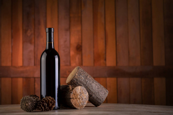 A selective focus shot of a wine bottle with pine cones and stumps on a wooden background - Foto, afbeelding