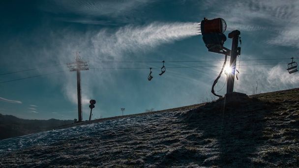 Güneşli bir günde kar topu silueti ya da kayak pistindeki yapay kar makinesi. Görünür güneş bir topun egzozunun arkasında parlıyor. - Fotoğraf, Görsel