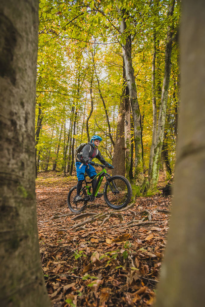 Radler, die im Herbst oder Winter im Wald mit einem modernen Elektrofahrrad oder Mountainbike bergauf fahren. Moderne E-Biker im Wald. - Foto, Bild