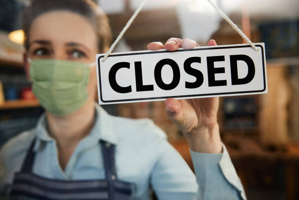 Female Owner Of Small Business Wearing Face Mask Turning Round Closed Sign During Health Pandemic - Foto, immagini