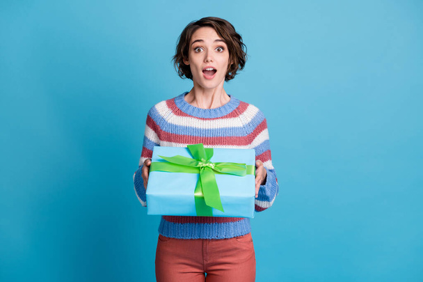 Photo portrait of amazed surprised girl holding gift with ribbon opened mouth isolated on bright blue color background - 写真・画像