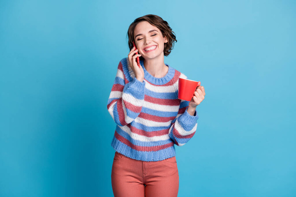 Photo portrait of laughing girl speaking on mobile phone keeping cup with drink isolated on vibrant blue color background - Foto, Imagem