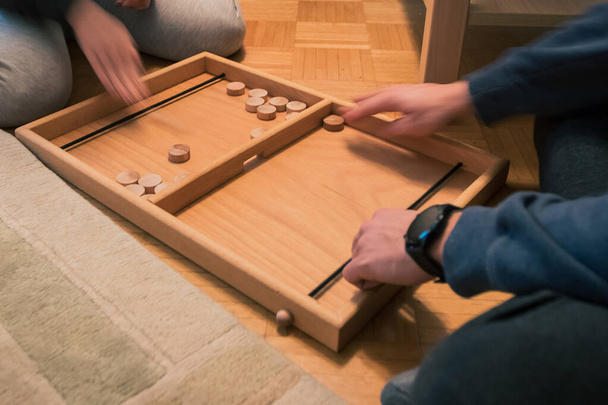 Wooden bard game where you shoot round wooden blocks through opening with help of an elastic band. Two players visible. - Photo, Image