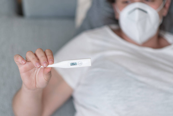 mujer enferma y embarazada en máscara médica sosteniendo termómetro digital - Foto, imagen