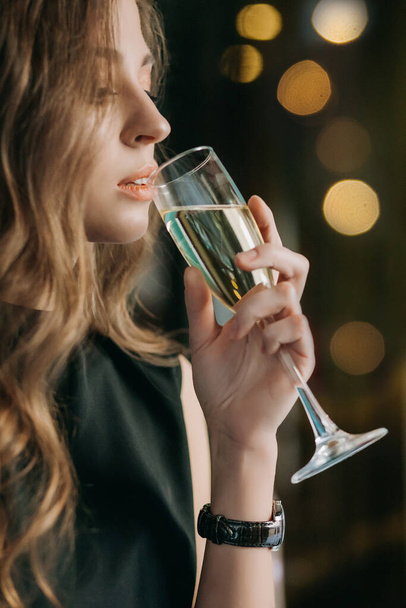 Romantic woman with long flying hair holds glass of champagne. Gorgeous long healthy hair. Blonde model with waving hair in black golf. Professional makeup, sexy sensual lips, open mouth - Φωτογραφία, εικόνα