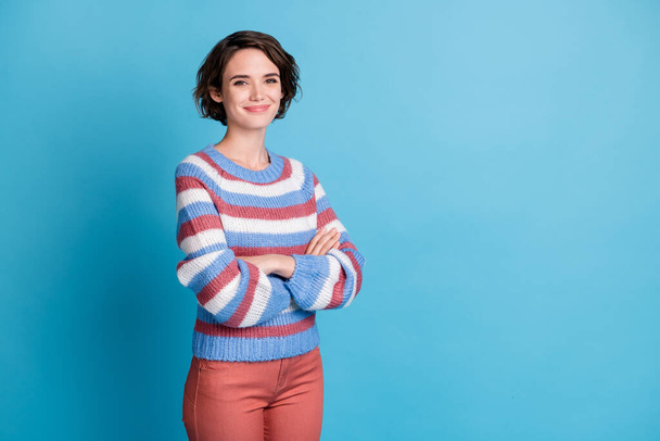 Photo of cute lady crossed hands look camera genuine smile wear colorful striped pullover red trousers isolated blue color background - 写真・画像