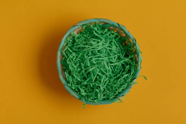 Green basket for easter eggs on a yellow background. Top view - Φωτογραφία, εικόνα