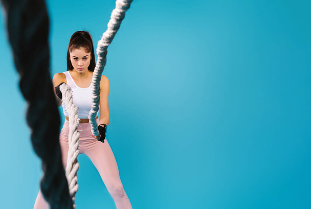 A studio photo in which a young, focused girl in leggings and a top throws ropes at the camera. Blue background and empty side ad space. - Foto, Imagem