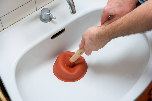 Caucasian male hand holding a plunger unclogging a bathroom sink. - Photo, Image