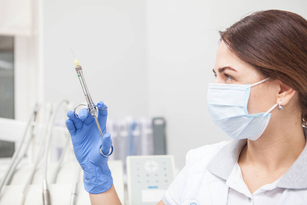 Close up of a female doctor wearing medical face mask, looking at the syringe she is holding - Фото, изображение
