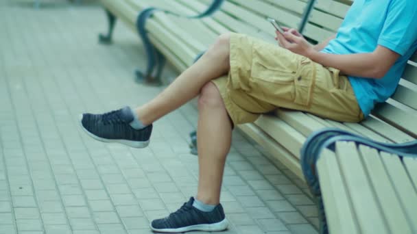 Piernas peludas de un hombre en pantalones cortos sentado en un banco, rastreando la cámara - Metraje, vídeo