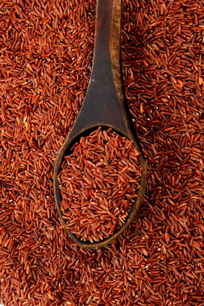Сирий червоний рис у старій дерев'яній ложці на фоні червоного рису. Коричневий рис в дерев'яній ложці
 - Фото, зображення