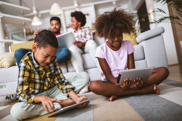 Ragazzo e ragazza afroamericani sdraiati sul pavimento e utilizzando tablet digitale. Famiglia a casa. - Foto, immagini