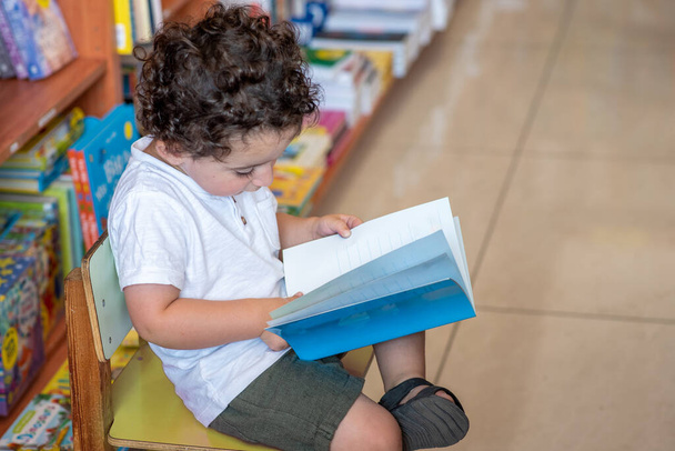 Menino adorável, sentado em uma livraria, lendo um livro. - Foto, Imagem