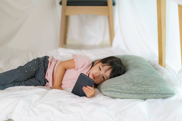 Азиатская милая маленькая девочка смотрит мультфильм в смартфоне, лежа в форте одеяло в гостиной у себя дома для идеального укрытия от других членов семьи и для них, чтобы играть творчески. - Фото, изображение