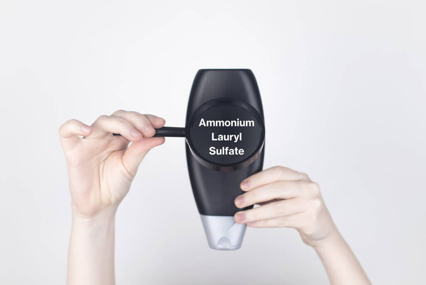 Composants chimiques sur l'étiquette du shampooing : Laurylsulfate d'ammonium. Les mains de la femme tiennent une loupe sur le bocal, ce qui indique l'ingrédient nocif. Fond blanc, place pour votre texte - Photo, image